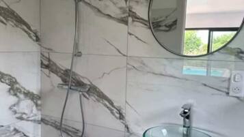Un baño con paredes de mármol, un lavabo de vidrio y un cabezal de ducha de mano.