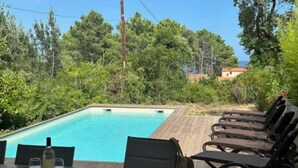 Un área de comedor junto a la piscina con una mesa dispuesta para dos personas, una botella de vino y un sombrero sobre la mesa.