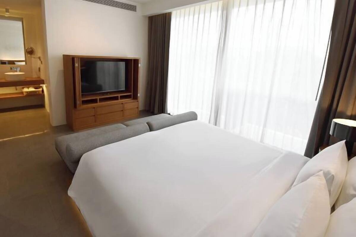 Habitación de hotel con una cama grande, televisión, un pequeño rincón de descanso y ventana con cortinas.