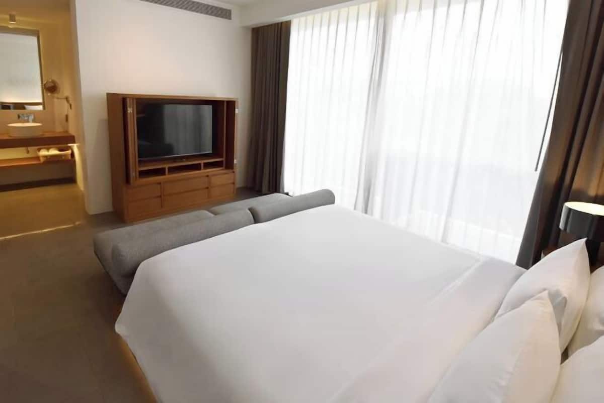 A hotel room with a large bed, a television, a small seating area, and a window with curtains.