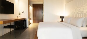 Ein Hotelzimmer mit einem großen Bett, einem an der Wand befestigten Fernseher, einem Schreibtisch mit Pflanze und einem Nachttisch mit Lampe.