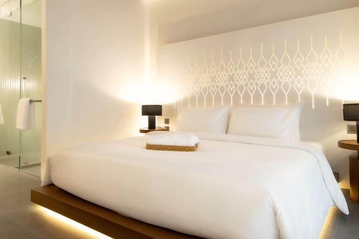 Una habitación de hotel moderna con una cama grande, cabina de ducha de vidrio y un panel decorativo en la pared.