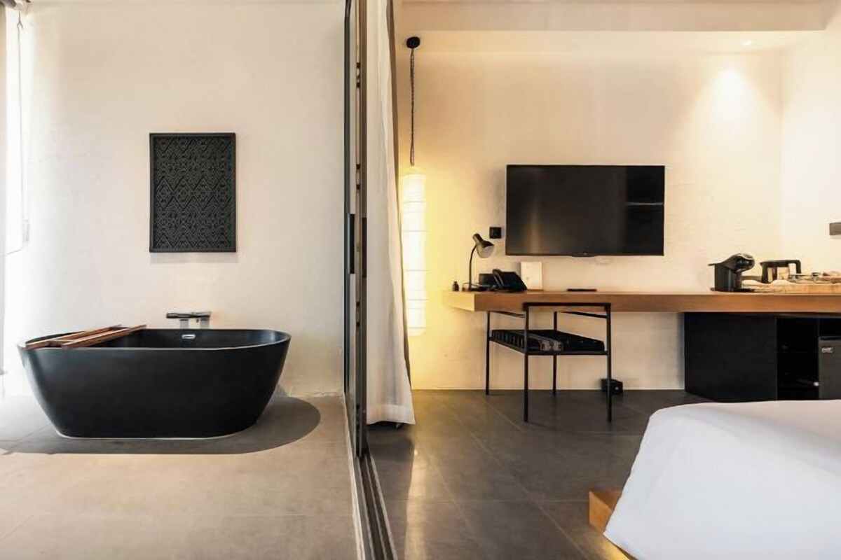 Una habitación de hotel moderna con una bañera negra grande, un escritorio de madera, un televisor de pantalla plana y una cama.
