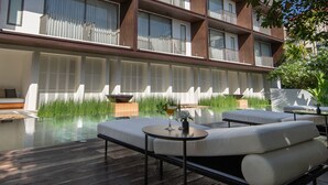 Un hotel moderno con piscina en la azotea, zona de estar al aire libre y barandilla de cristal.