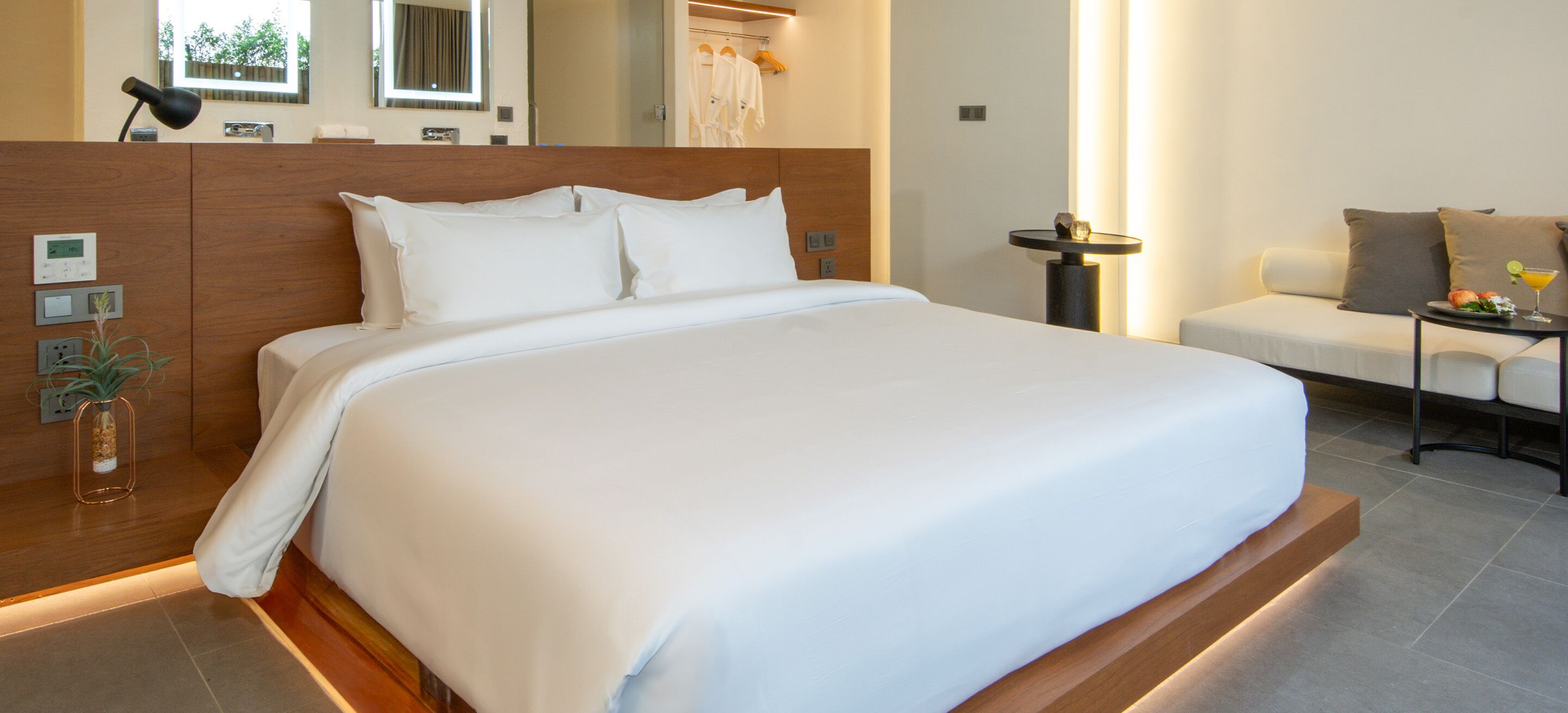 A modern hotel room with a large bed, bedside table, and a seating area with a table and chairs.