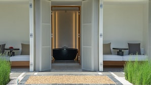 A modern spa area with a large black bathtub, two white sofas with cushions, and a small table with a red object on it. - Arun Khiri Chiang Mai Hotel (Chiang Mai)