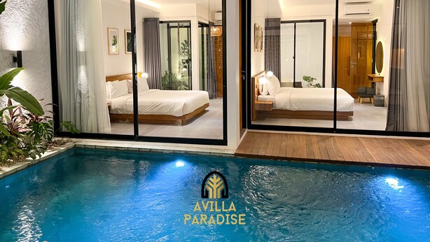 Quarto de hotel moderno com uma cama grande, mesa de cabeceira e vista para a piscina.