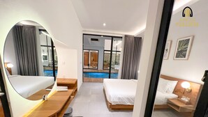 Quarto de hotel com cama, escrivaninha, um banco, espelho e vista para uma piscina ao ar livre.
