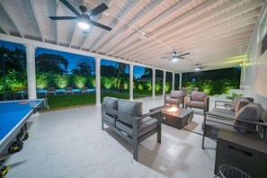 An outdoor patio area with a pool table, sofas, and a fire pit.