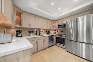 A modern kitchen with stainless steel appliances, wooden cabinets, and a white countertop.