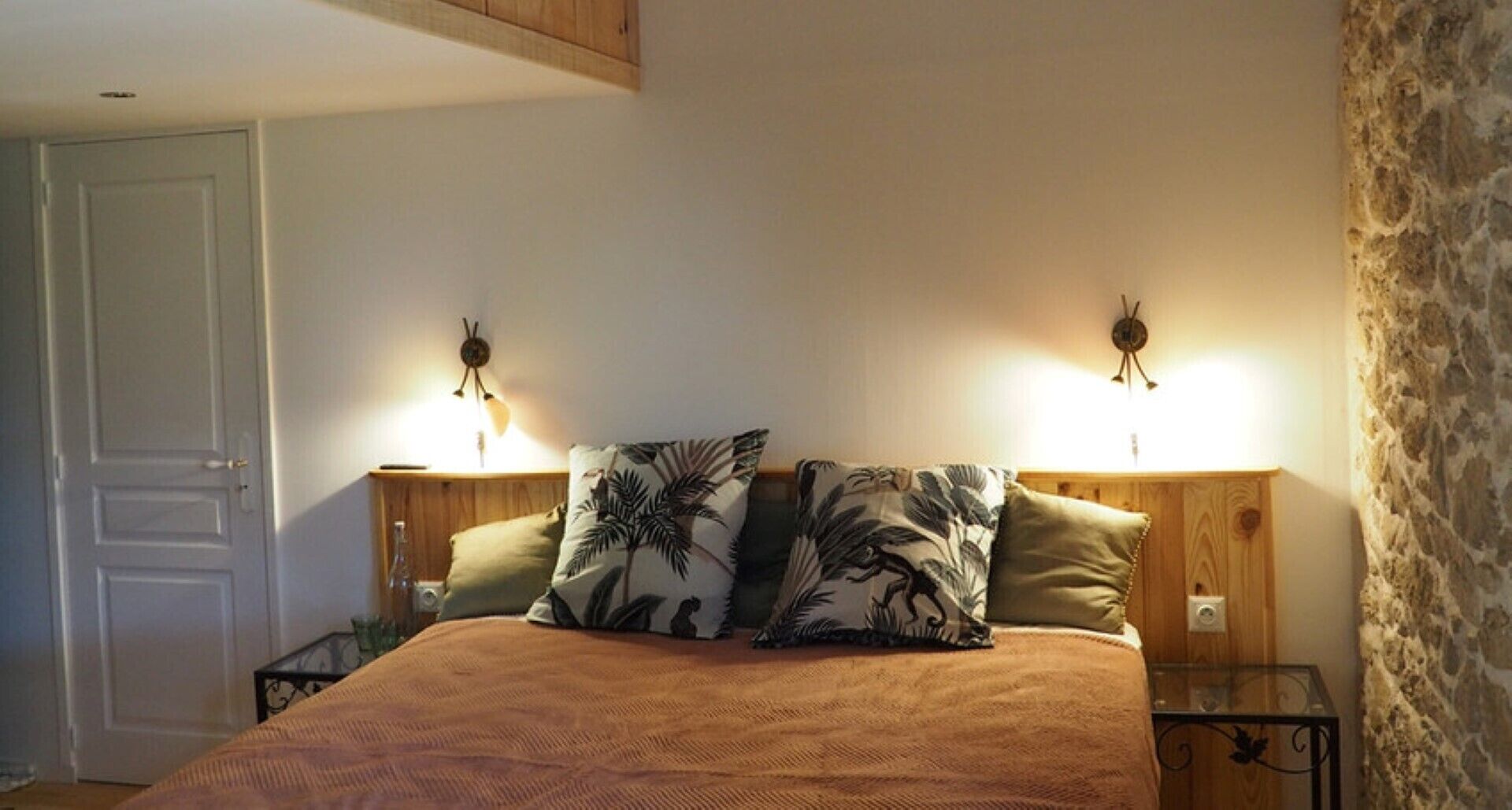 A bedroom with a bed, two nightstands, a wooden headboard, and two wall-mounted lamps.