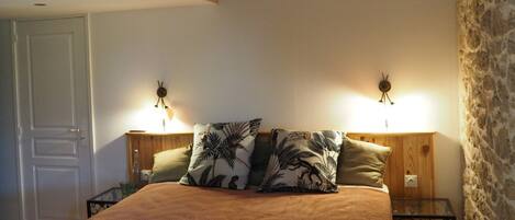 A bedroom with a bed, two nightstands, a wooden headboard, and two wall-mounted lamps.
