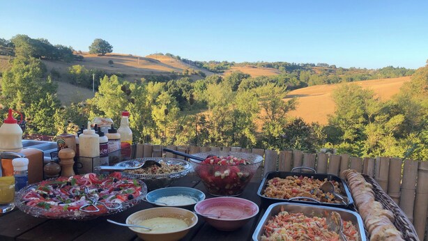 A picnic table with various food items and condiments, set against a backdrop of a scenic landscape.
