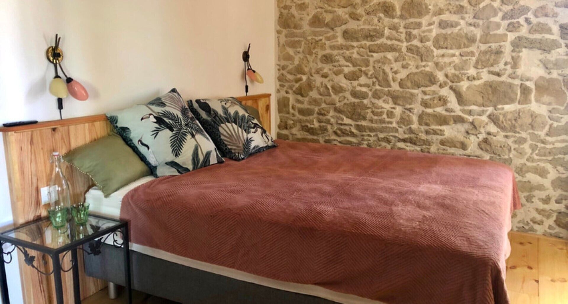 Une chambre à coucher avec un lit, une table de chevet, une bouteille et des verres.