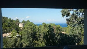 A view from a window overlooking a forested area with a stone tower and a body of water in the distance. - Villa Panoramique Piscine Chauffee 4 CH +4 SDB (SARI SOLENZARA)