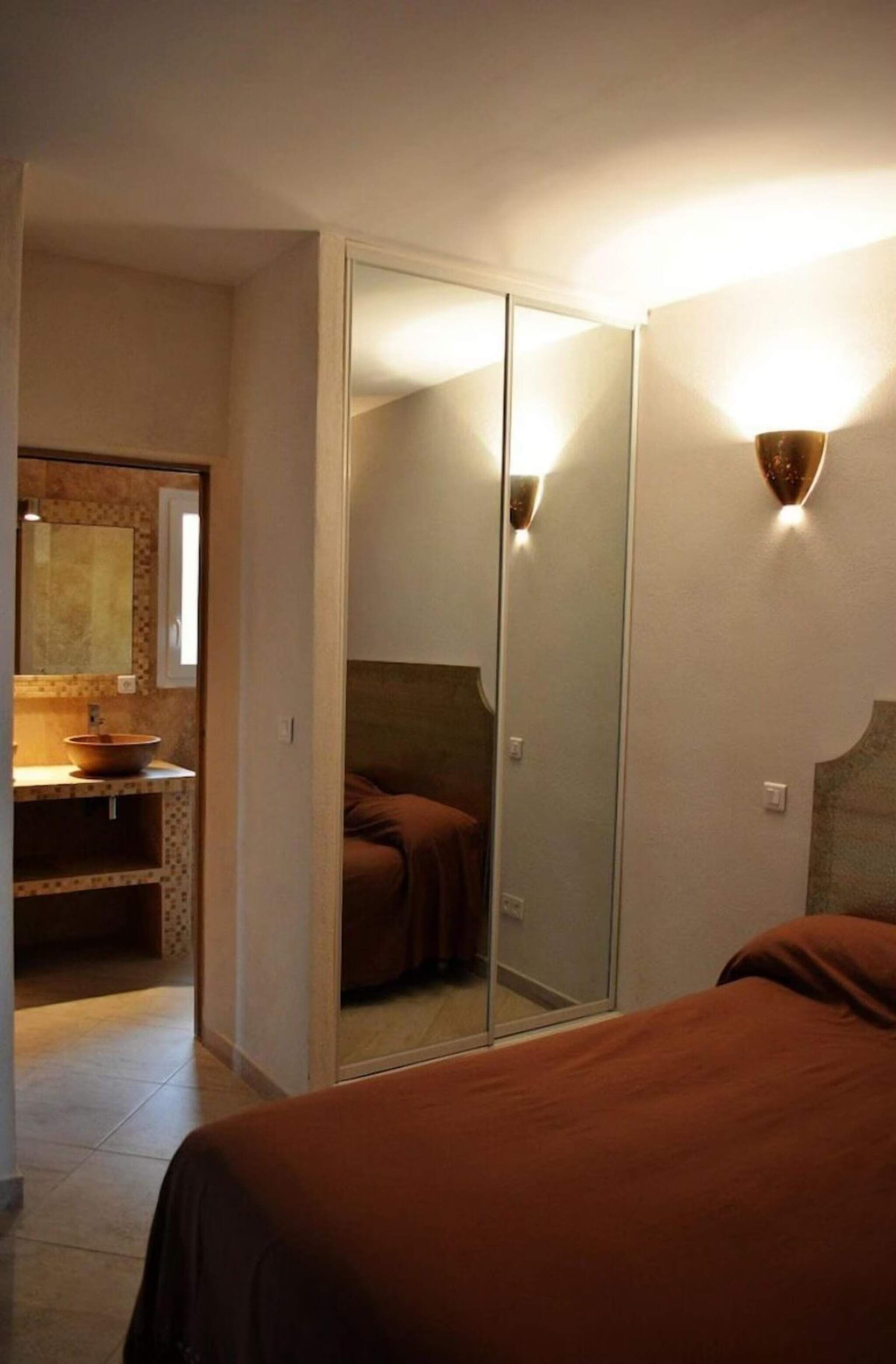 Un dormitorio con un espejo grande, una mesita de noche y una colcha marrón.