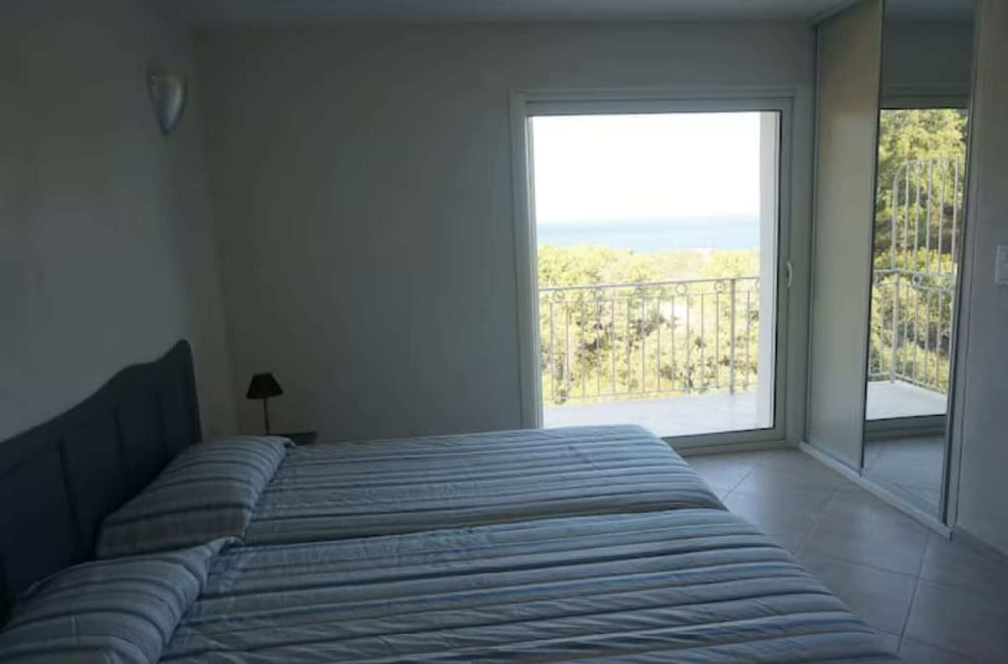 Une chambre avec un grand lit, une table de chevet et une vue sur un balcon doté d’une balustrade et bordé d’arbres.