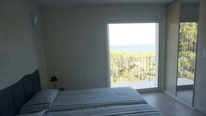 A bedroom with a large bed, a nightstand, and a view of a balcony with a railing and trees. - Villa Panoramique Piscine Chauffee 4 CH +4 SDB (SARI SOLENZARA)