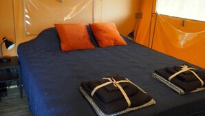 A bed with a blue mattress, two orange pillows, and two folded towels with a leopard print pattern and beige ties. - Glamping Lodge Monet | Domaine du Cammazet | Pool| Comfort | Nature (Lapenne)