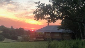 En etagers bygning med fladt tag, omgivet af grønt, og en solnedgang i baggrunden.