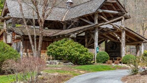 A rustic log cabin with a steeply pitched roof, a chimney, and a porch supported by wooden beams. - Spring Brook Mountain Retreat + Hot Tub +Sauna+ Fire Pit (Mars Hill)