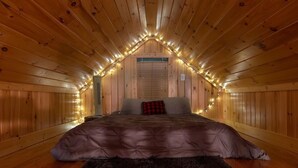 A cozy attic bedroom with wooden walls and a sloped ceiling, featuring a bed with a dark-colored comforter and a red and black checkered pillow. - Spring Brook Mountain Retreat + Hot Tub +Sauna+ Fire Pit (Mars Hill)