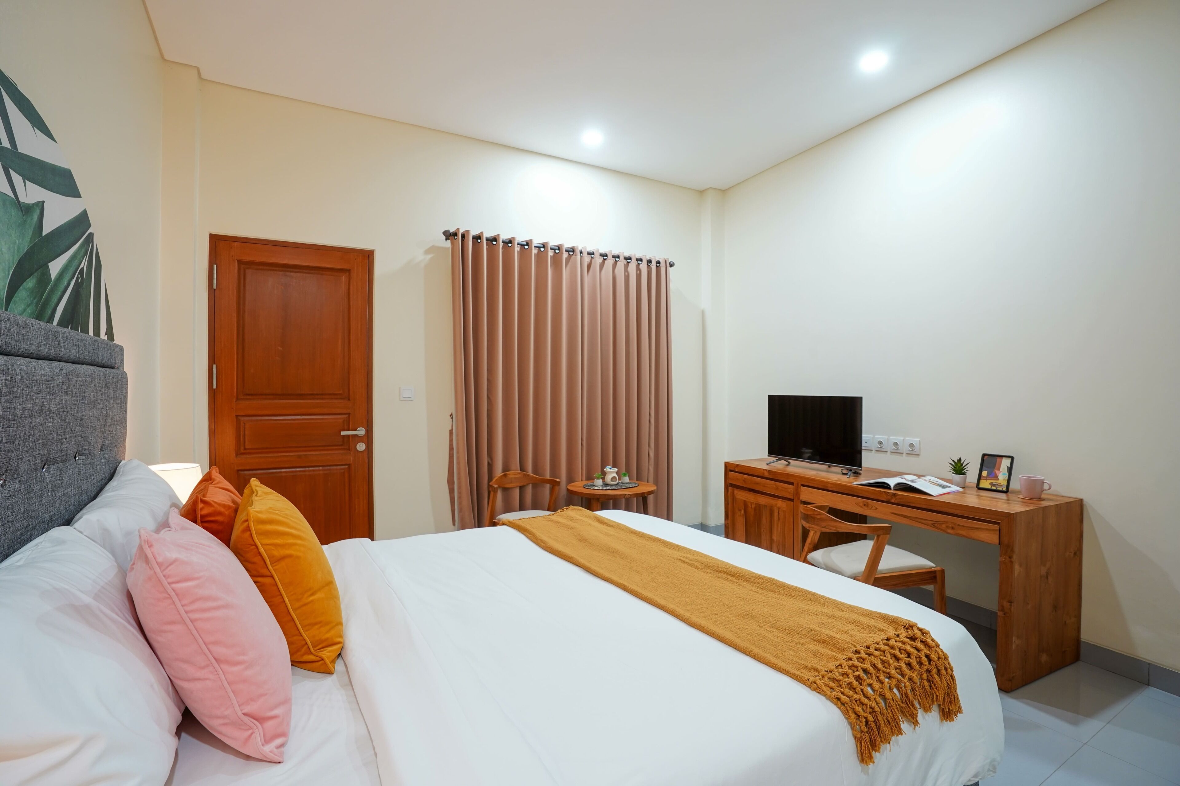 A bedroom with a bed, a desk, a chair, a television, and a door.