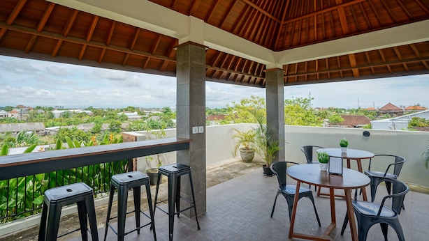 A covered outdoor area with a wooden ceiling, a table with chairs, and a view of the surrounding landscape. - Cove Griya Elite (Denpasar)