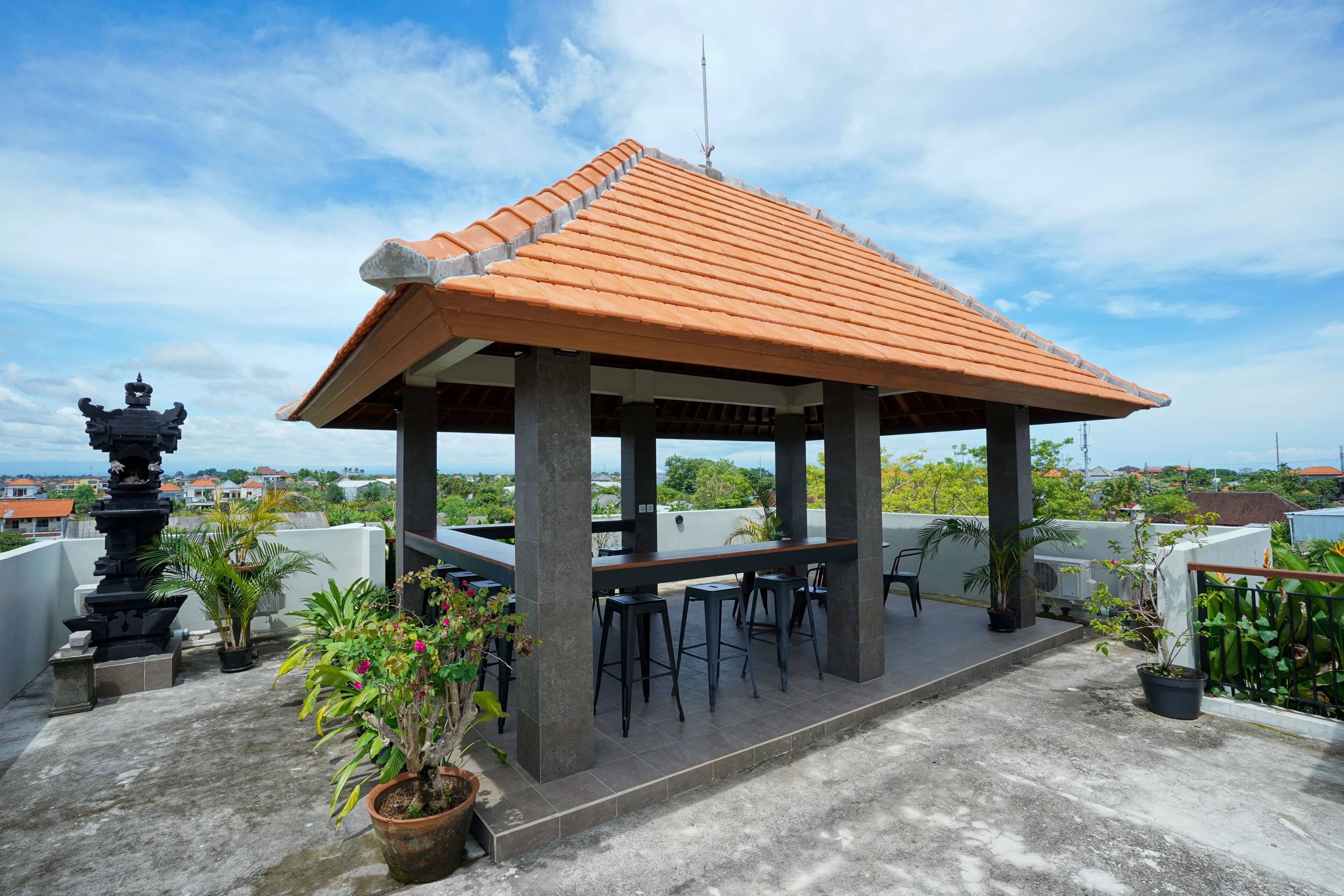 A rooftop terrace with a tiled roof, concrete pillars, and a seating area with bar stools.