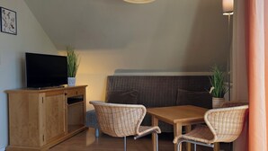 Un salon confortable avec un canapé, un téléviseur posé sur un meuble en bois, des fauteuils en osier et une table.