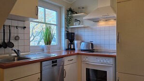 Une cuisine moderne équipée d’un lave-vaisselle, d’un four et d’une fenêtre donnant sur les arbres.