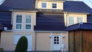 Une maison à deux étages, avec un toit en tuiles, une porte d’entrée et un petit jardin.