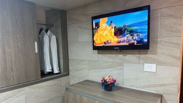 Un baño moderno con tocador de madera, un espejo, televisor de pantalla plana y un florero con flores.