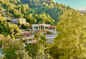 A building with a stone facade, green shutters, and a balcony overlooking a lush, green hillside.