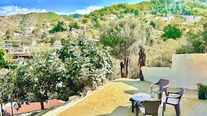 Terraza en la azotea con mesa y sillas, rodeada de árboles y vistas a un pueblo en la ladera.