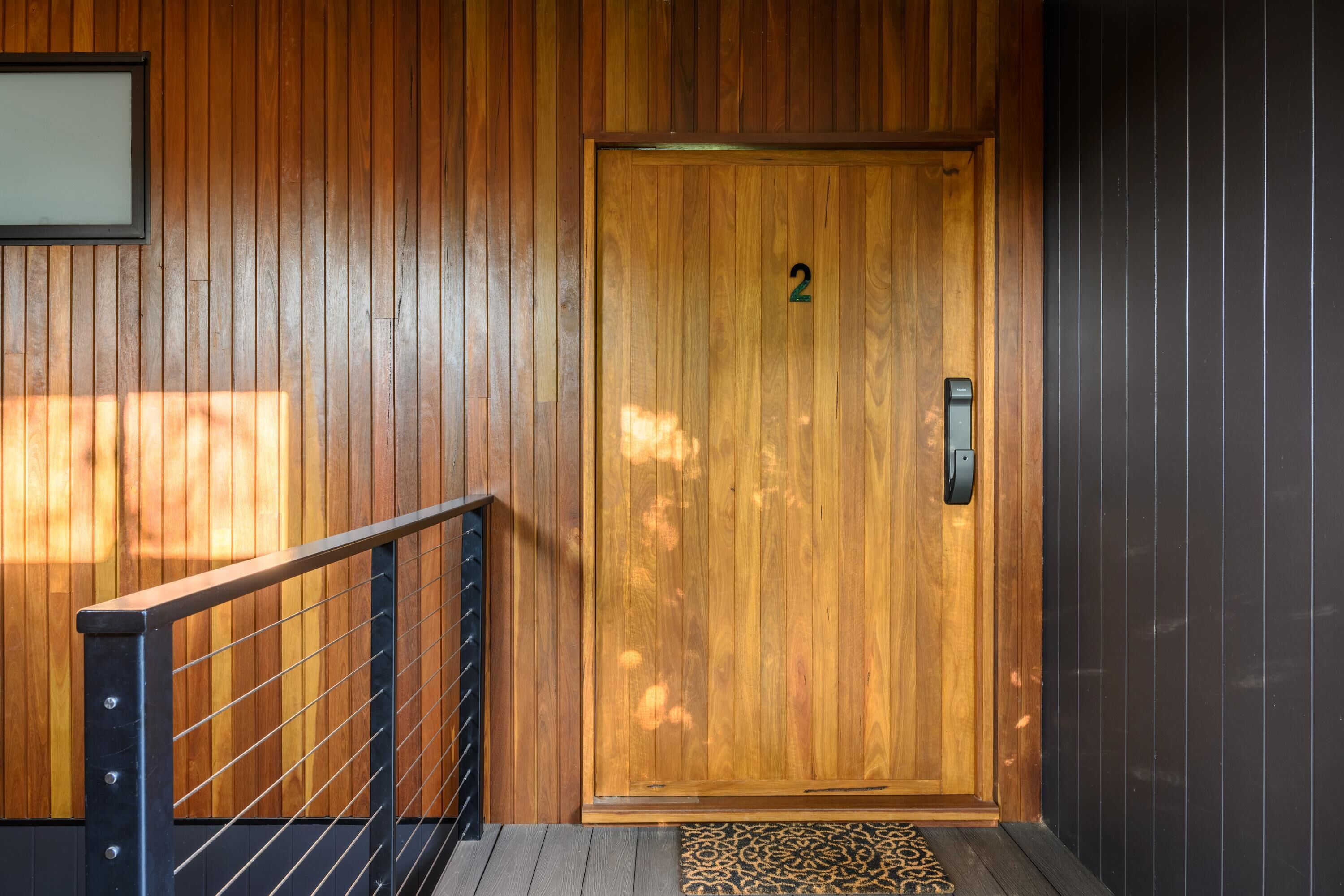 A wooden door with a number "2" above it, a metal handrail, and a patterned mat at the entrance.