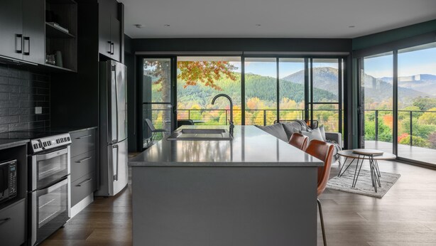 A modern kitchen with a large island, built-in appliances, and a view of a mountainous landscape through large windows. - The View Bright - Apartment 2 - The View Bright has a fabulous outlook and location, being one of the few places in the Bright township with uninterrupted views of the Upper Ovens Valley and Mount Bogong. (Bright)