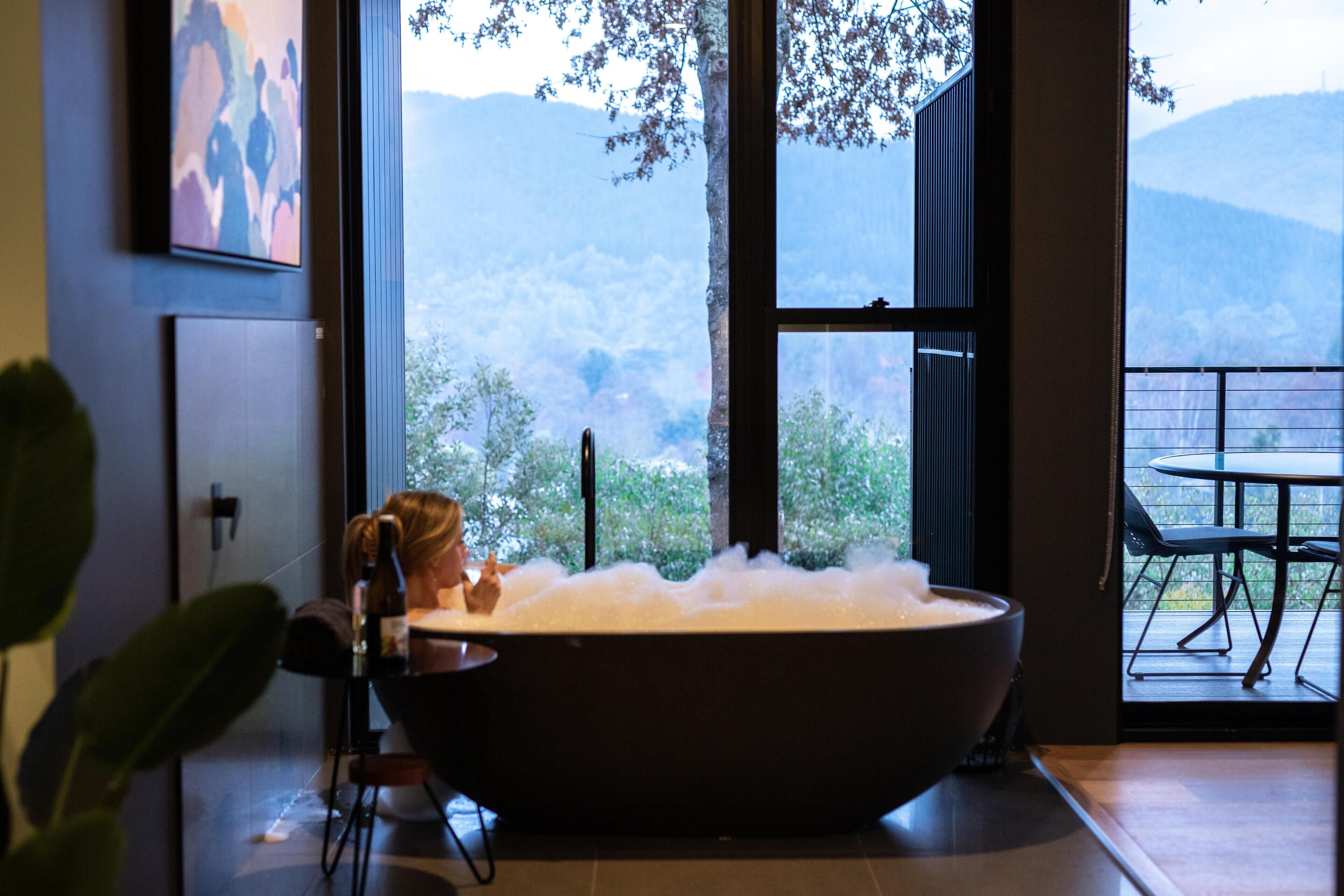 A large bathtub with a view of mountains through a large window.