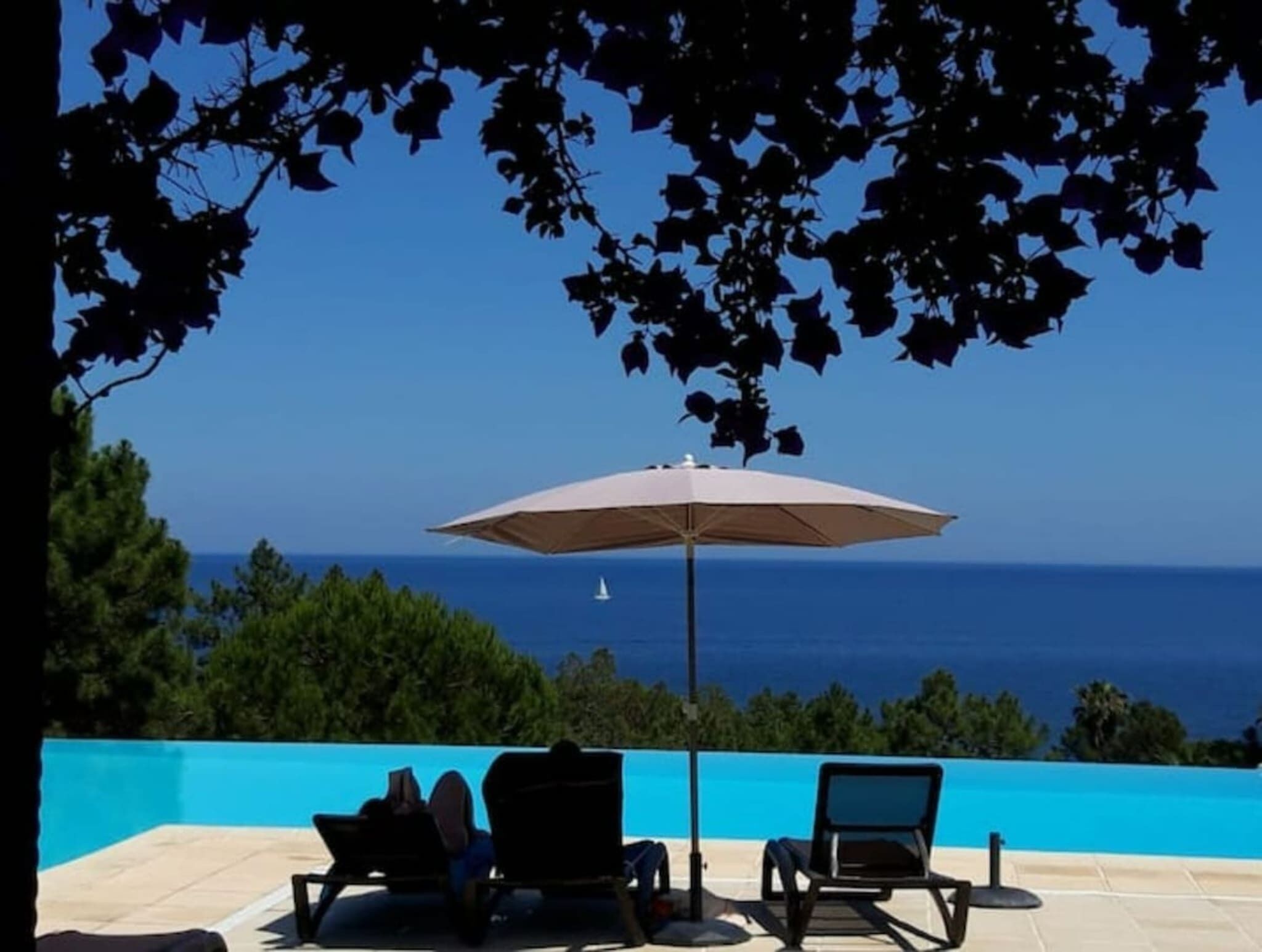 A poolside area with two lounge chairs and an umbrella, overlooking a clear blue sky and ocean.