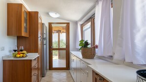A kitchen with wooden cabinets, a stainless steel refrigerator, a fruit bowl, and a window with curtains. - Sant'Anna house on Brionis estate with large veranda overlooking the sea (Alghero)