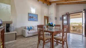 A dining area with a wooden table and chairs, a white sofa, and a painting of a coastal scene. - Sant'Anna house on Brionis estate with large veranda overlooking the sea (Alghero)