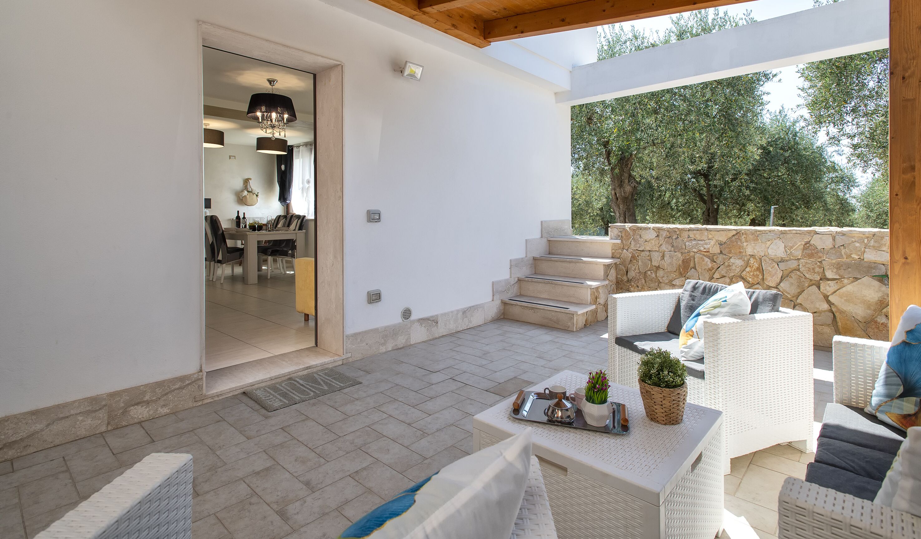 A modern outdoor patio with wicker furniture, a stone wall, and a view of trees.