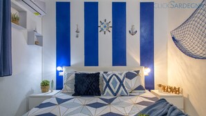 Een slaapkamer met een bedovertrek met geometrisch patroon, een wandklok en een kleine plant in een potje op het nachtkastje.