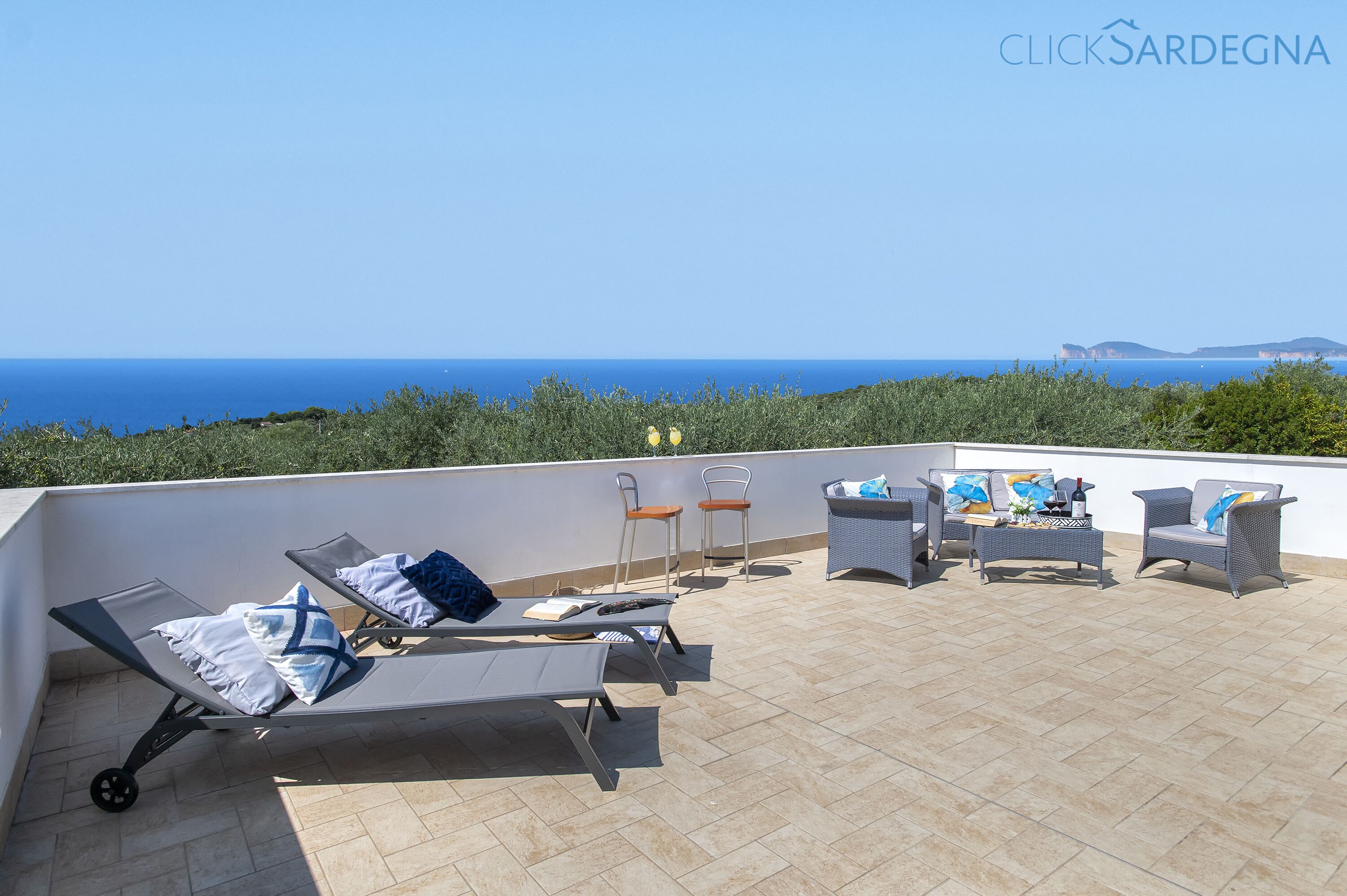 A rooftop terrace with lounge chairs, a table, and chairs overlooking the sea.