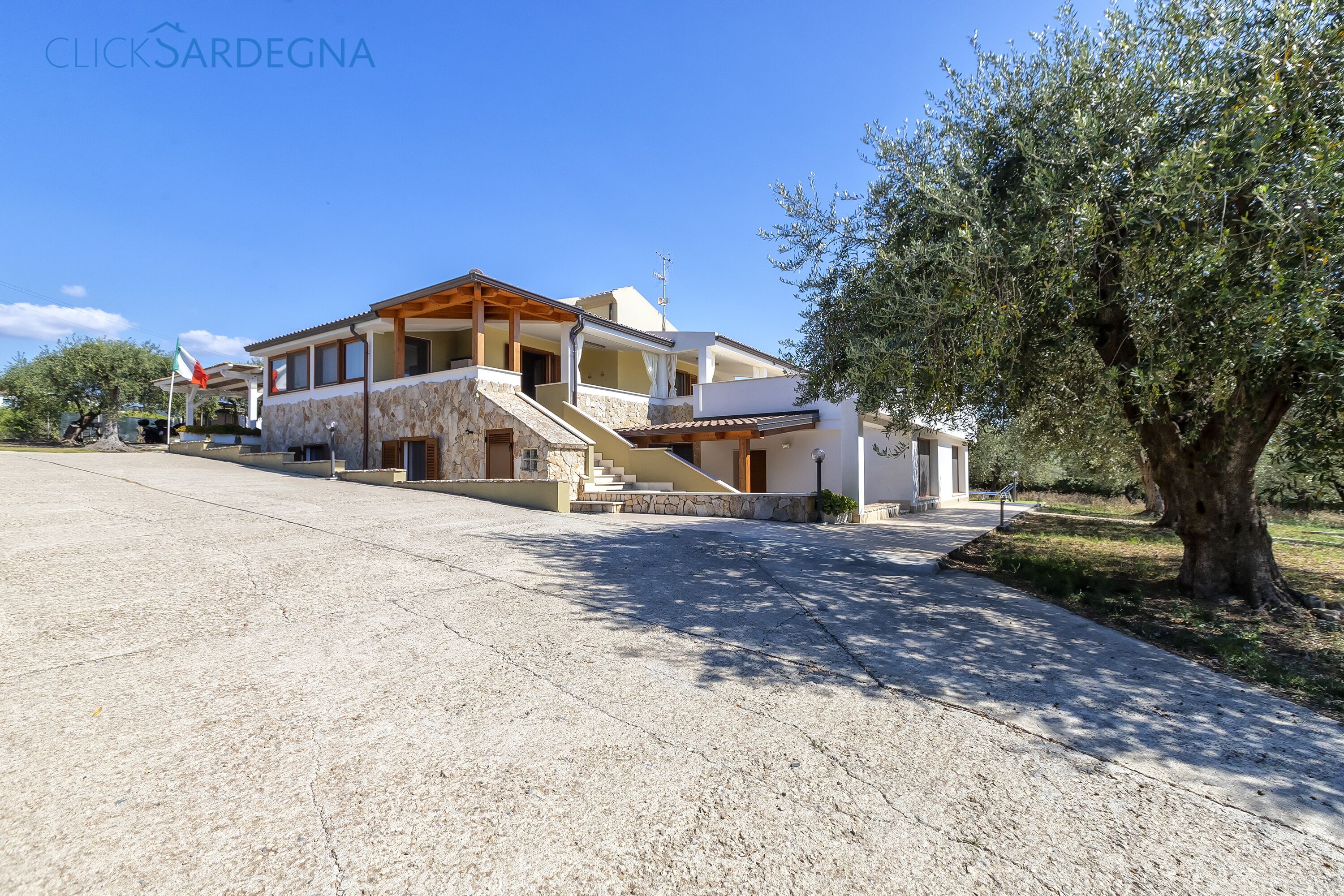 A modern house with a stone facade, a wooden balcony, and a large tree in the foreground.