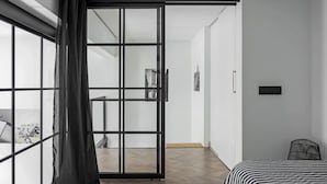 A modern bedroom with a large sliding glass door leading to a balcony, a bed with a striped bedspread, and a black chair. - Lux apartment in Minsk (Minsk)