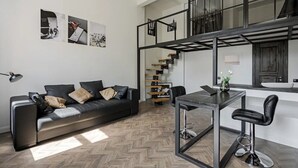 A modern living space with a black leather sofa, a herringbone wood floor, a dining table with bar stools, and a staircase with a black metal frame. - Lux apartment in Minsk (Minsk)