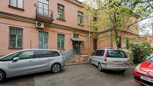 A building with a red brick facade, a staircase leading to a door, and two parked cars. - Lux apartment in Minsk (Minsk)