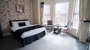 A hotel room with a large bed, a small table, two chairs, and a balcony with curtains. - The Spread Eagle (Manchester)