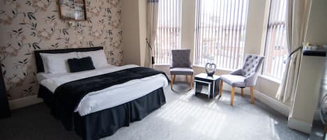 A hotel room with a large bed, a small table, two chairs, and a balcony with curtains.